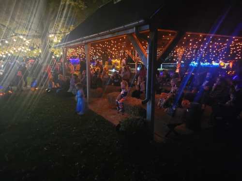 A festive outdoor gathering under a lit pavilion, with people enjoying the evening atmosphere and decorations.