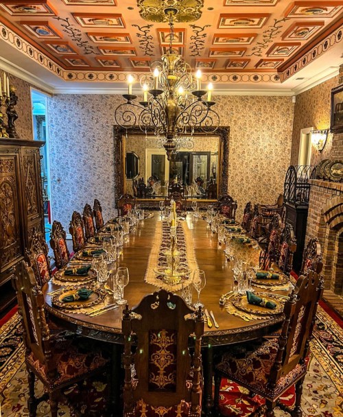 Elegant dining room with a long table set for a formal meal, ornate decor, and a chandelier overhead.