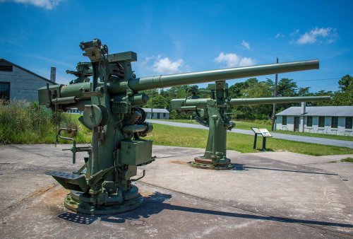 Two large military cannons on concrete pads, set against a clear blue sky and grassy landscape.