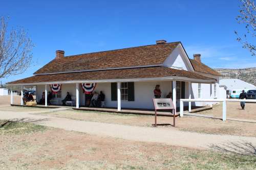 A historic building with a porch, decorated with red, white, and blue bunting, surrounded by a grassy area.