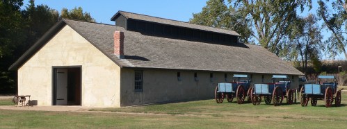 Historic building with a sloped roof, surrounded by green grass and several blue wagons lined up in front.