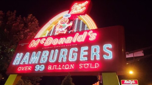 Bright neon sign for McDonald's featuring "HAMBURGERS" and "Over 99 billion sold" at night.