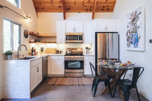Modern kitchen with white cabinets, stainless steel appliances, and a dining table set for two with fruit.