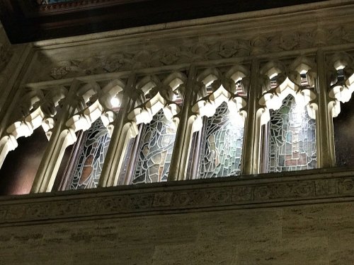 Stained glass windows with intricate designs, illuminated from below, set in a stone wall with Gothic architectural details.