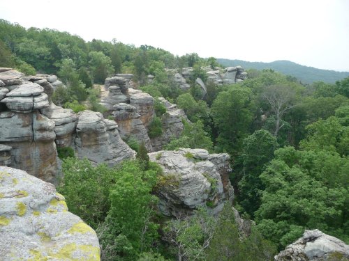 A scenic view of rocky cliffs surrounded by lush green trees and distant hills under a cloudy sky.