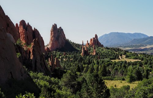 A scenic view of red rock formations surrounded by greenery and mountains under a clear blue sky.