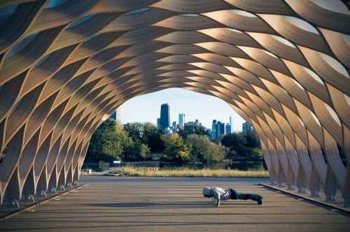 A person doing push-ups under a wooden archway, with a city skyline visible in the background.