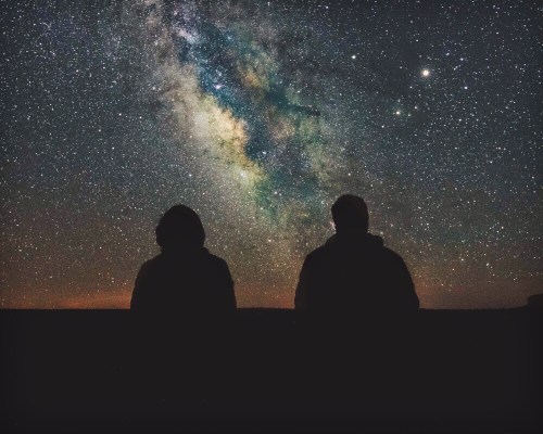 Silhouettes of two people gazing at a starry night sky filled with the Milky Way.