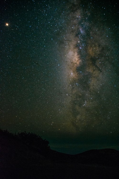 A stunning view of the Milky Way galaxy filled with stars, set against a dark night sky and silhouetted hills.