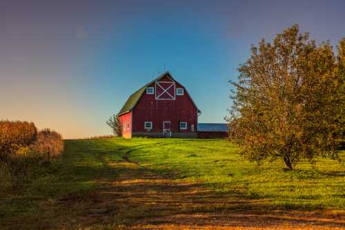 A red barn on a grassy hill, surrounded by trees and fields under a clear blue sky.