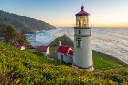 A scenic lighthouse on a cliff overlooking the ocean, surrounded by lush greenery and a sunset sky.