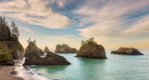 Scenic coastal view with rocky islands, lush trees, and a calm sea under a cloudy sky.