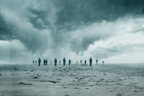 Silhouettes of figures walking on a desolate landscape under a dramatic, cloudy sky.
