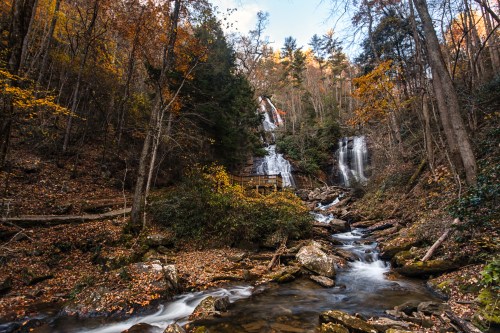 A serene waterfall surrounded by autumn foliage and a flowing stream in a forested landscape.