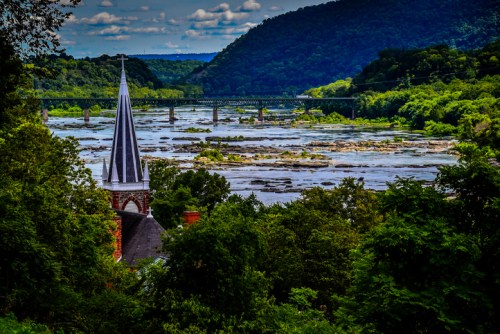 A scenic view of a river with a bridge, surrounded by lush greenery and a church steeple in the foreground.