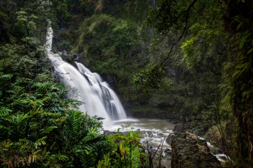 A serene waterfall cascades down rocky terrain, surrounded by lush green foliage and misty air.