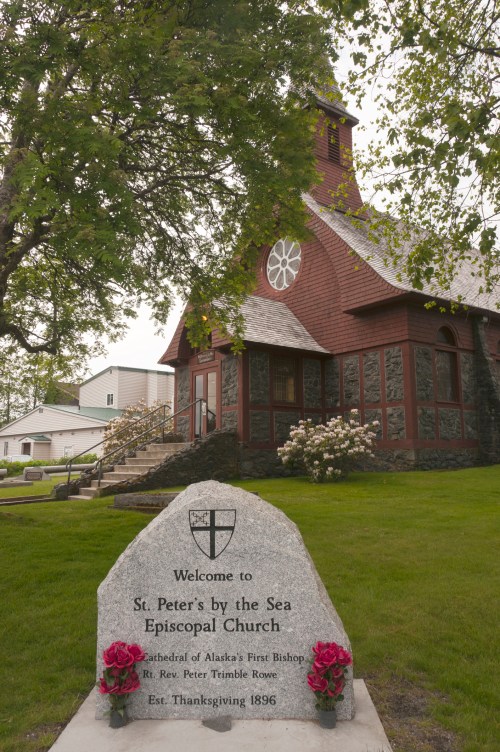 A stone sign welcomes visitors to St. Peter's by the Sea Episcopal Church, with a historic building in the background.