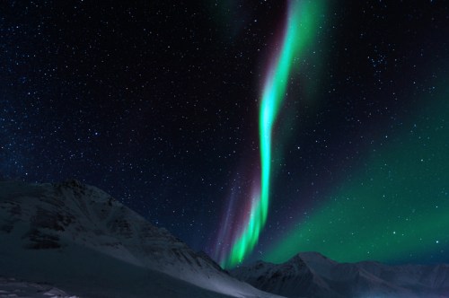 A stunning display of the Northern Lights illuminates the night sky over snow-capped mountains.