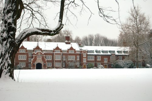 A large brick building covered in snow, surrounded by trees and a white landscape on a winter day.