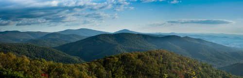 Panoramic view of rolling green mountains under a blue sky with scattered clouds.