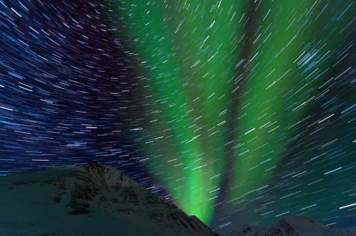 A stunning display of the Northern Lights with vibrant green hues illuminating the night sky over snowy mountains.
