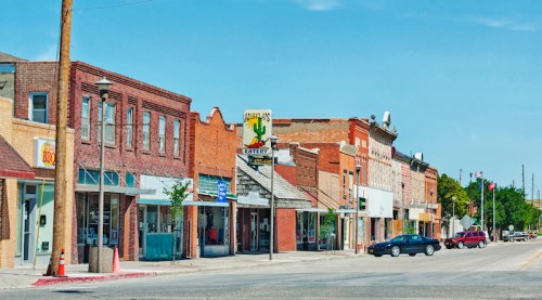 A sunny street view of a small town with brick buildings, shops, and a cactus-themed sign.