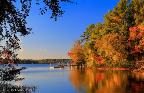A serene lake scene with colorful autumn trees reflecting in the water and a wooden dock in the background.