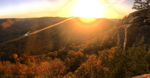 A stunning sunset over a valley, with vibrant autumn foliage and a river winding through the landscape.
