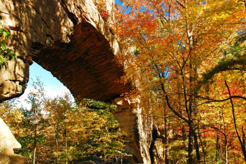 A natural stone arch surrounded by vibrant autumn foliage and clear blue skies.