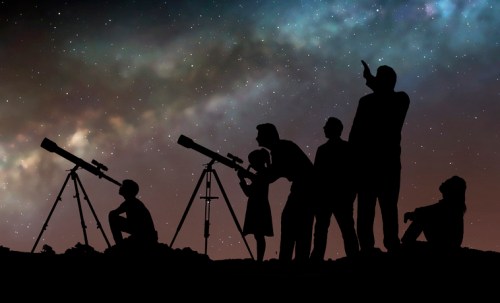 Silhouettes of people observing the night sky with telescopes against a starry backdrop.