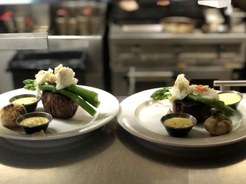 Two plates of gourmet steak topped with crab, asparagus, and sauces, served with garlic mashed potatoes.