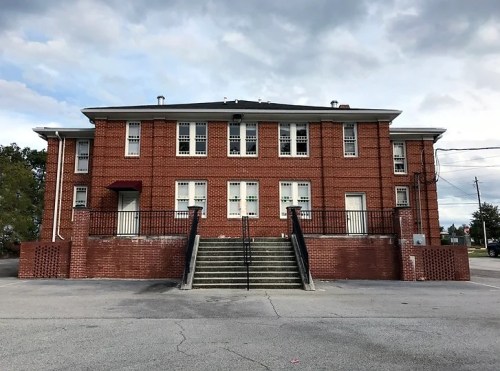 A brick building with multiple windows and a staircase leading to the entrance, set against a cloudy sky.