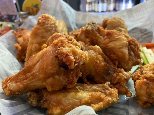A close-up of a basket filled with crispy, golden-brown fried chicken wings on parchment paper.