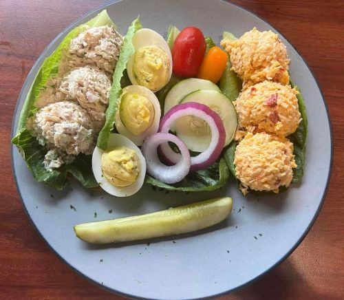 A plate with lettuce wraps filled with chicken salad, sliced eggs, tomatoes, onions, and a pickle.