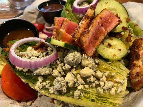 A fresh salad with romaine lettuce, grilled chicken, cucumbers, tomatoes, red onions, bacon, and blue cheese crumbles.