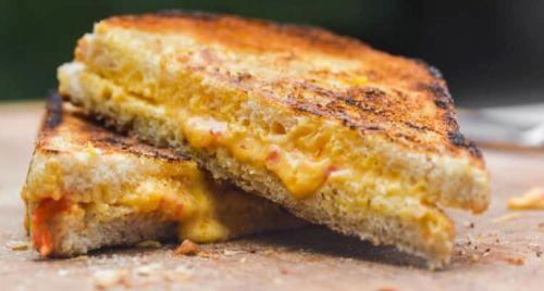 A close-up of a grilled cheese sandwich, golden brown and oozing melted cheese, cut in half on a wooden surface.