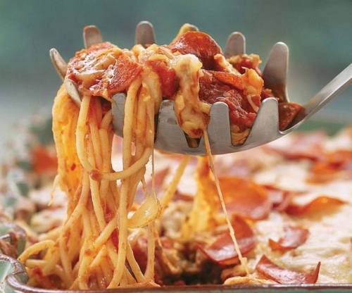A serving of spaghetti topped with pepperoni being lifted from a baking dish with a spatula.