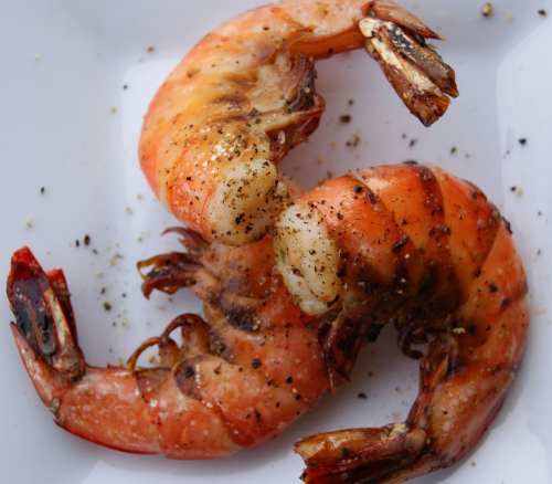 Two grilled shrimp seasoned with black pepper on a white plate.