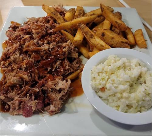 A plate with pulled pork in barbecue sauce, seasoned fries, and a side of creamy coleslaw.