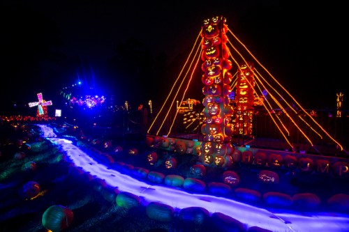 A vibrant display of illuminated pumpkins and colorful lights along a winding path at night.