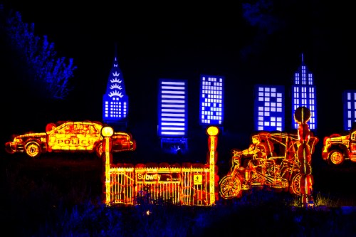 Colorful light display featuring police cars, skyscrapers, and a subway entrance against a dark background.