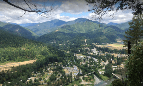 A scenic view of a valley surrounded by mountains, with a small town and river visible below.