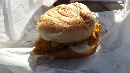 A sesame seed bun sandwich with a crispy fried chicken fillet and lettuce, wrapped in white paper.
