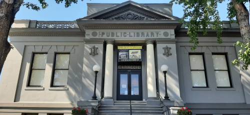 Front view of a Carnegie public library with steps, large windows, and decorative architectural details.