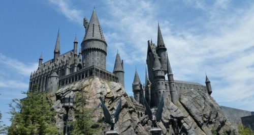 A majestic black castle with tall spires, perched on a rocky outcrop under a blue sky with scattered clouds.