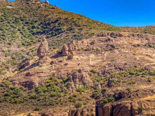 Rocky hillside with unique rock formations and sparse vegetation under a clear blue sky.