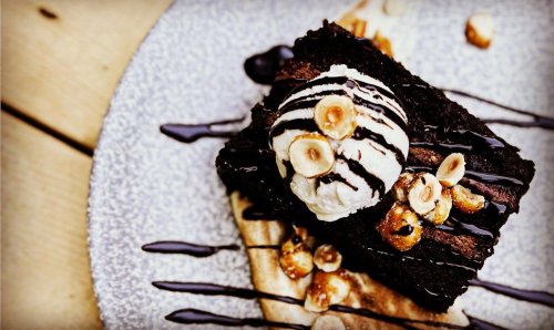A decadent chocolate brownie topped with vanilla ice cream, drizzled with chocolate sauce and sprinkled with hazelnuts.