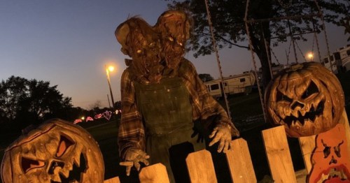 A spooky scarecrow figure with a twisted face stands near carved pumpkins at dusk, creating a Halloween atmosphere.
