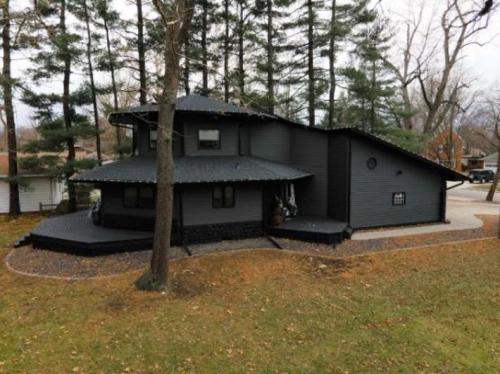 A modern black house surrounded by trees, featuring a unique architectural design and a landscaped yard.