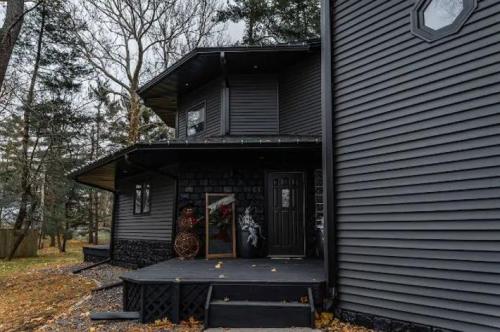 A modern black house with a unique design, featuring a porch and surrounded by trees in an autumn setting.